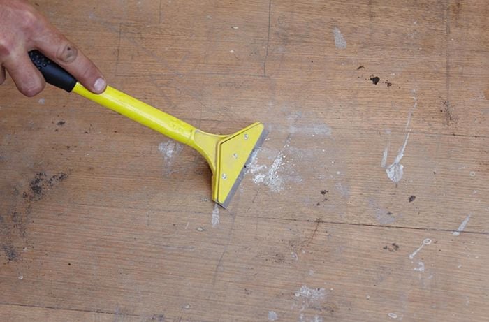 A scraper being used to remove old plaster from bare floorboards