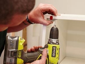 Person attaching a push-to-open mechanism at the top edge of a cabinet