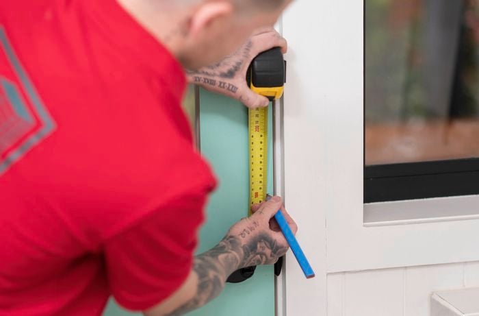 A Bunnings Team Member is measuring a door frame with a tape measure and marking it with a pencil.