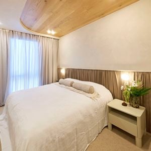 A furnished bedroom with a side table with a vase on it next to the bed and a bed head behind the bed, with carpet on the floor.