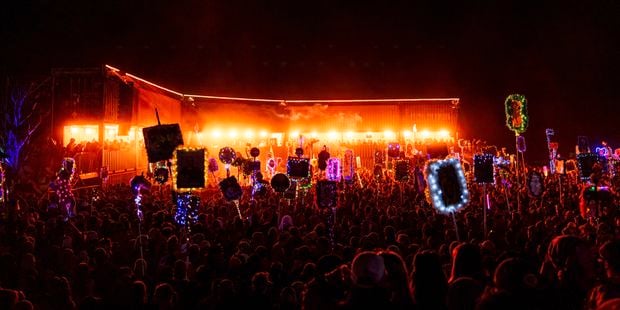 Night festival crowd holding colorful illuminated signs near a bright stage.