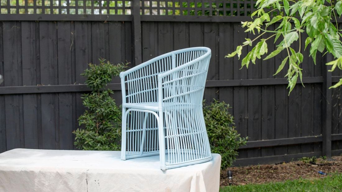 Painted wicker chair in gloss sky bus perched on a table covered in a drop sheet in a backyard
