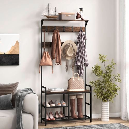 A black coat rack with scarves, handbags and shoes on it in a room with a couch, print on the wall and a vase ini it.
