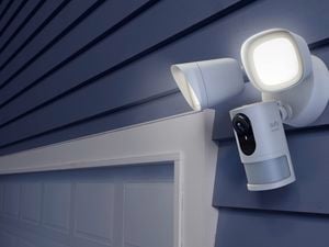 Eufy security camera with two floodlights mounted above a garage door on a house exterior.