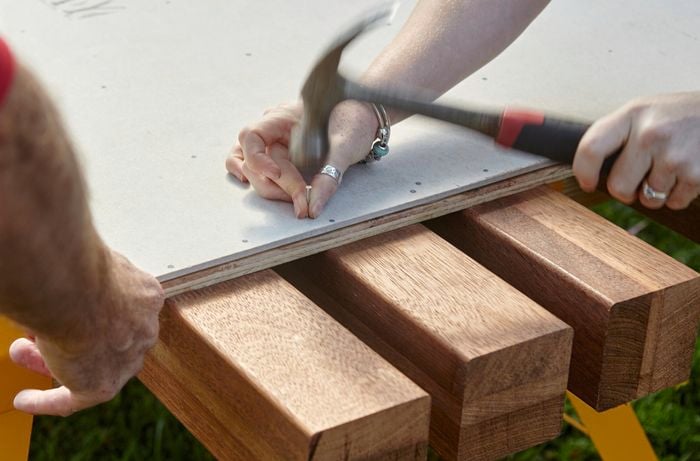 Person hammering cement sheeting to plywood.