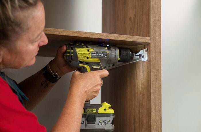 A Bunnings Team Member holding a cordless drill, drilling a screw into a shelving unit