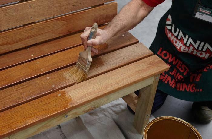 Person painting DIY wooden garden bench with varnish.
