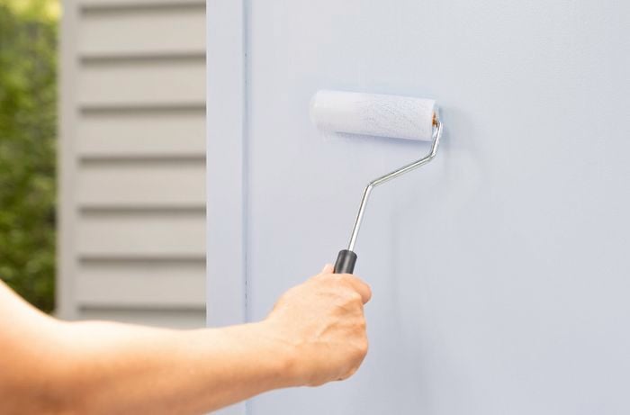 Paint roller applying a light blue coat of paint to the side panel of a cabinet.