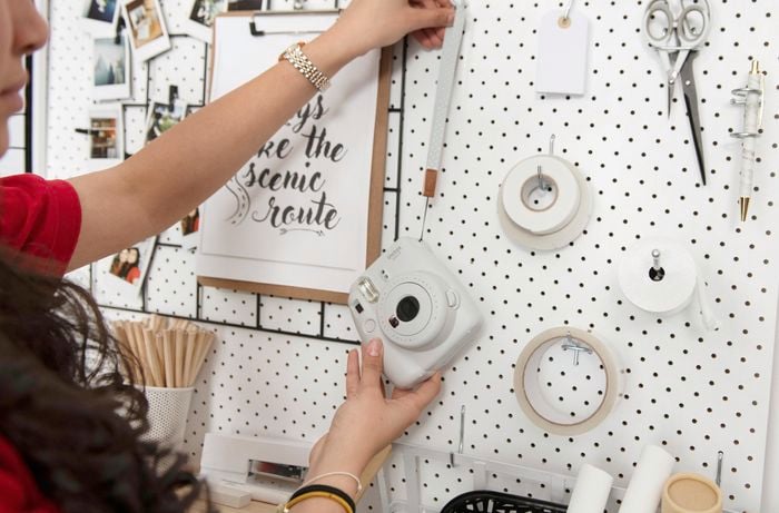 Person hanging camera from hook in pegboard wall.