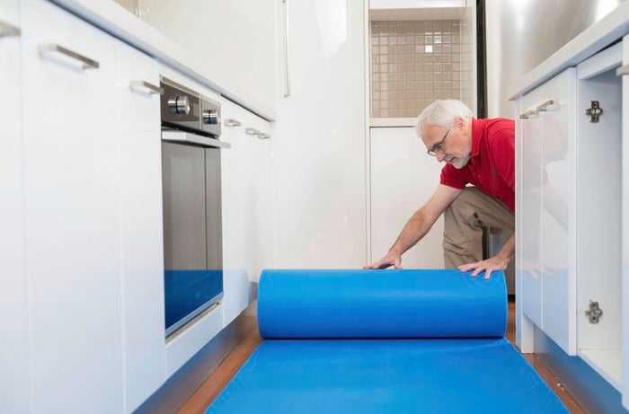 A Bunnings Team Member is laying a blue protective mat on the kitchen floor to keep your flooring safe from dust, scratches and falling debris. 