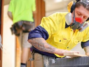 "Two people working with wood; one using a table saw while wearing safety gear in a workshop setting