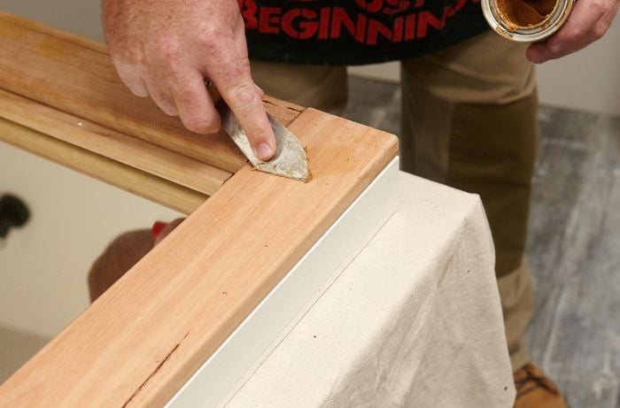 A person filling a gap in a piece of timber using wood filler