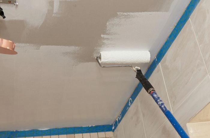 A ceiling being painted with an extension roller, with masking tape around the wall edges