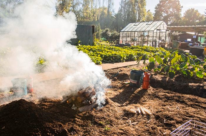Logs stacked on top of a dirt patch, with smoke coming out of the pile.