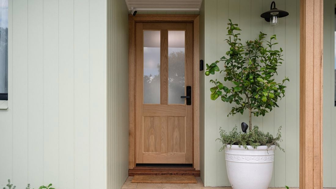 A green house with a timber front door and a plant at the front