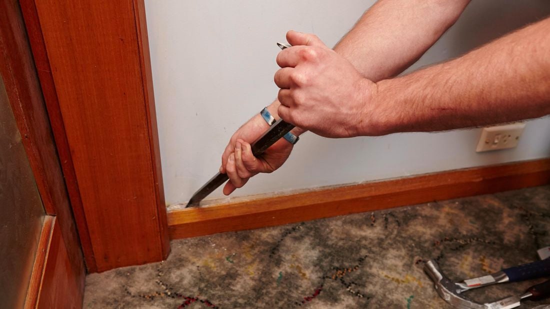 A person prising off a skirting board using a wrecking bar