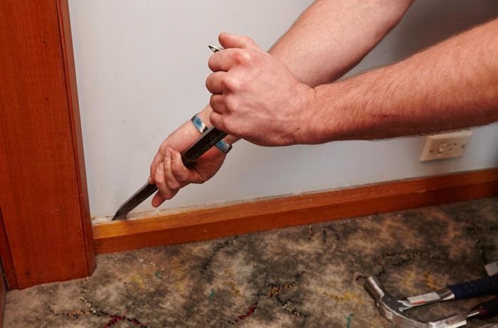 A person prising off a skirting board using a wrecking bar