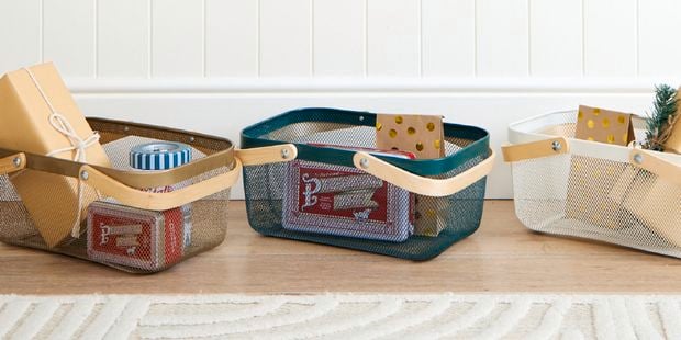 Three mesh baskets differing in colour with wooden handles, containing various wrapped gifts.