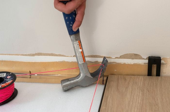 A hammer is removing a nail holding a pink stringline used as a straight guide. 