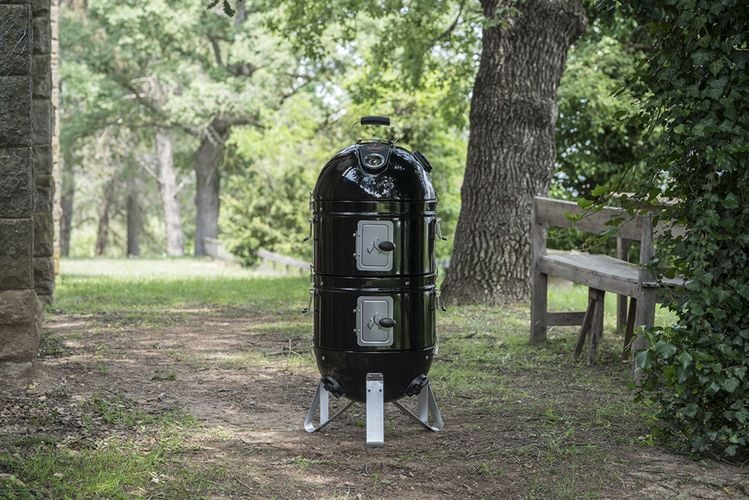 A black upright bullet smoker in a forested area