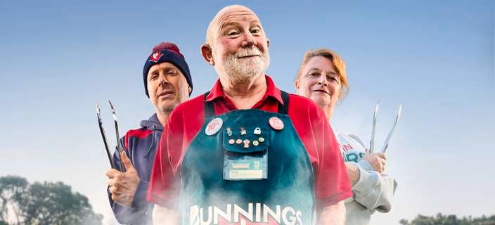 A Bunnings Team Member and 2 people in front of a BBQ with food on top of it.