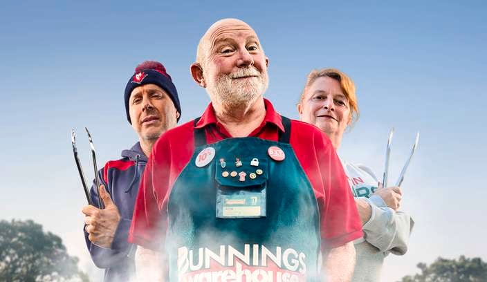 A Bunnings Team Member and 2 people in front of a BBQ with food on top of it.