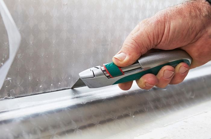 A person trimming frosting along the edge of a window using a trimming knife