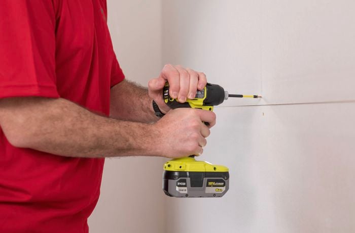 A Bunnings Team Member is inserting screws into the plasterboard with a drill driver. 