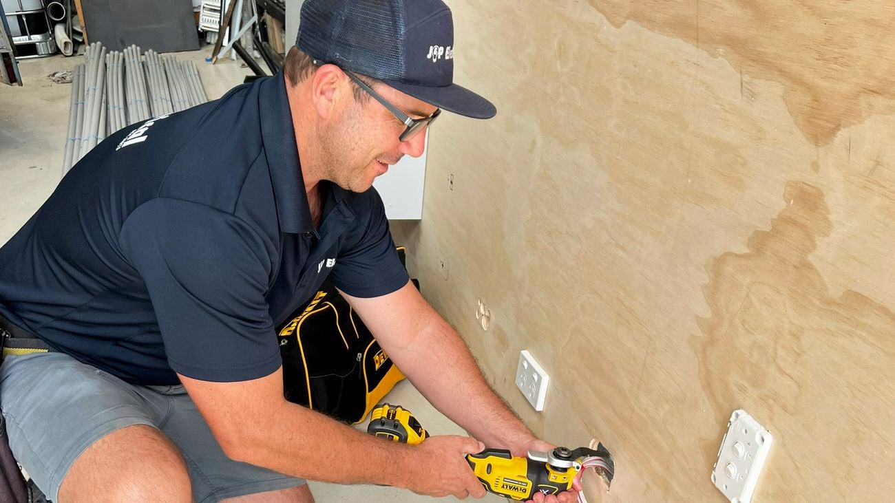 An electrician wearing a navy cap and shirt using a DeWALT multi-tool works on a power point