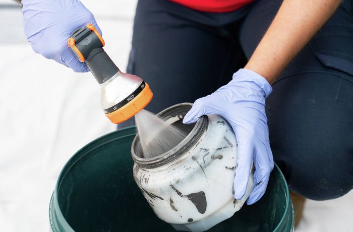 A person is cleaning a paint spray gun after painting a timber fence​​​ 