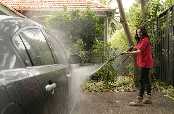 A cheerful woman standing and washing the exterior of the car with a pressure washer