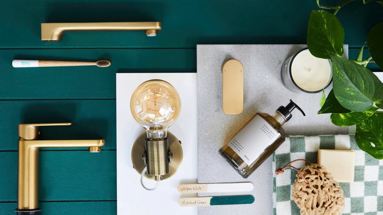 A contemporary bathroom flatlay. Brass sink mixers, tap and bathroom accessories on a VJ panel painted in Dulux Highland Green