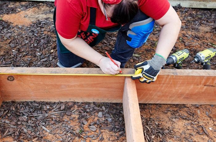 The framework of a sleeper compost bin being measured and marked with a tape measure and pencil