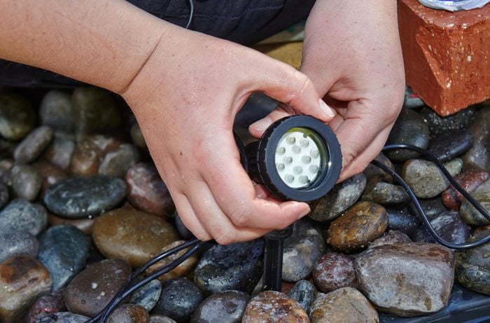 A person screwing the outer cover at the front of a pond light