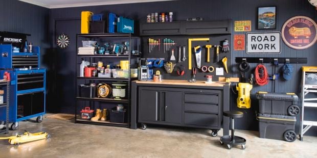 A garage with workbenches, storage cabinets, tools and old signs hanging on the walls.