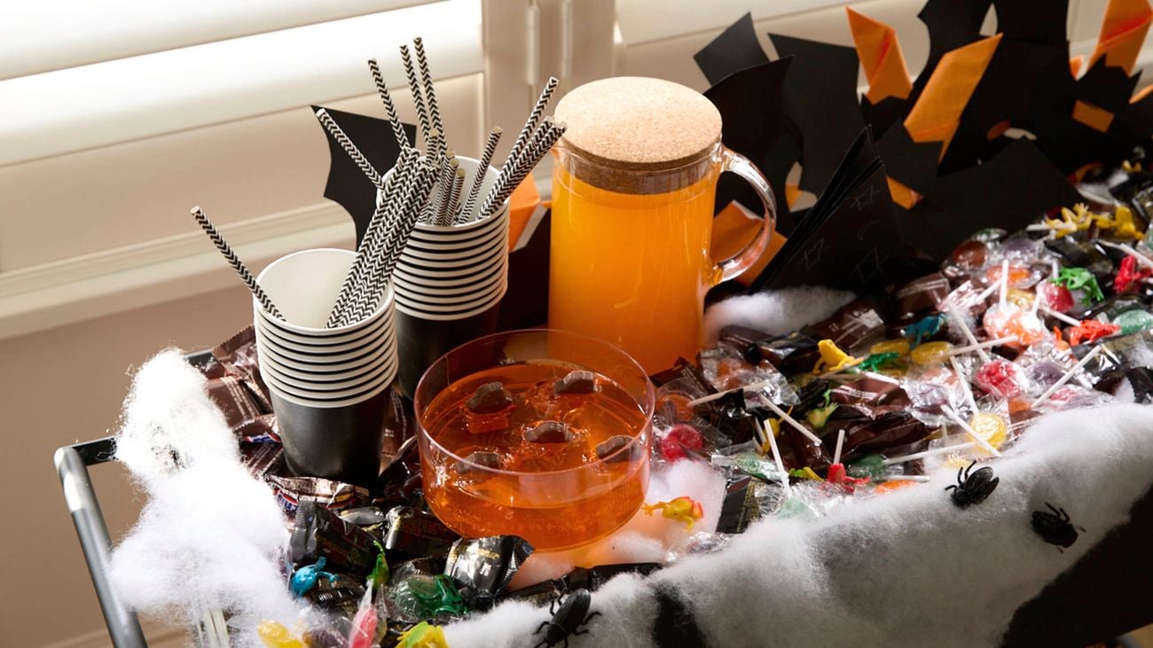A black plant trolley decorated with Halloween-themed items, including spiderweb fabric, bat cutouts, and orange pumpkin buckets filled with treats.