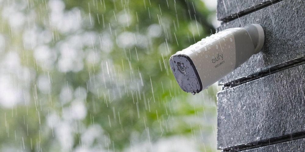 eufy security camera outside mounted to a gray wall in the rain.