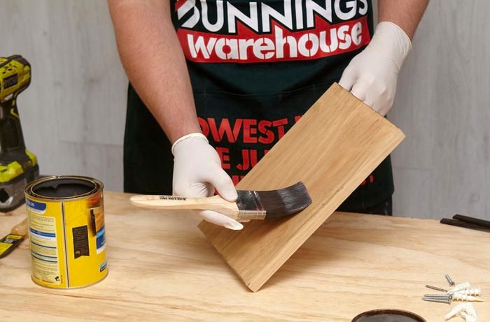 A person coating a small timber shelf with clear varnish