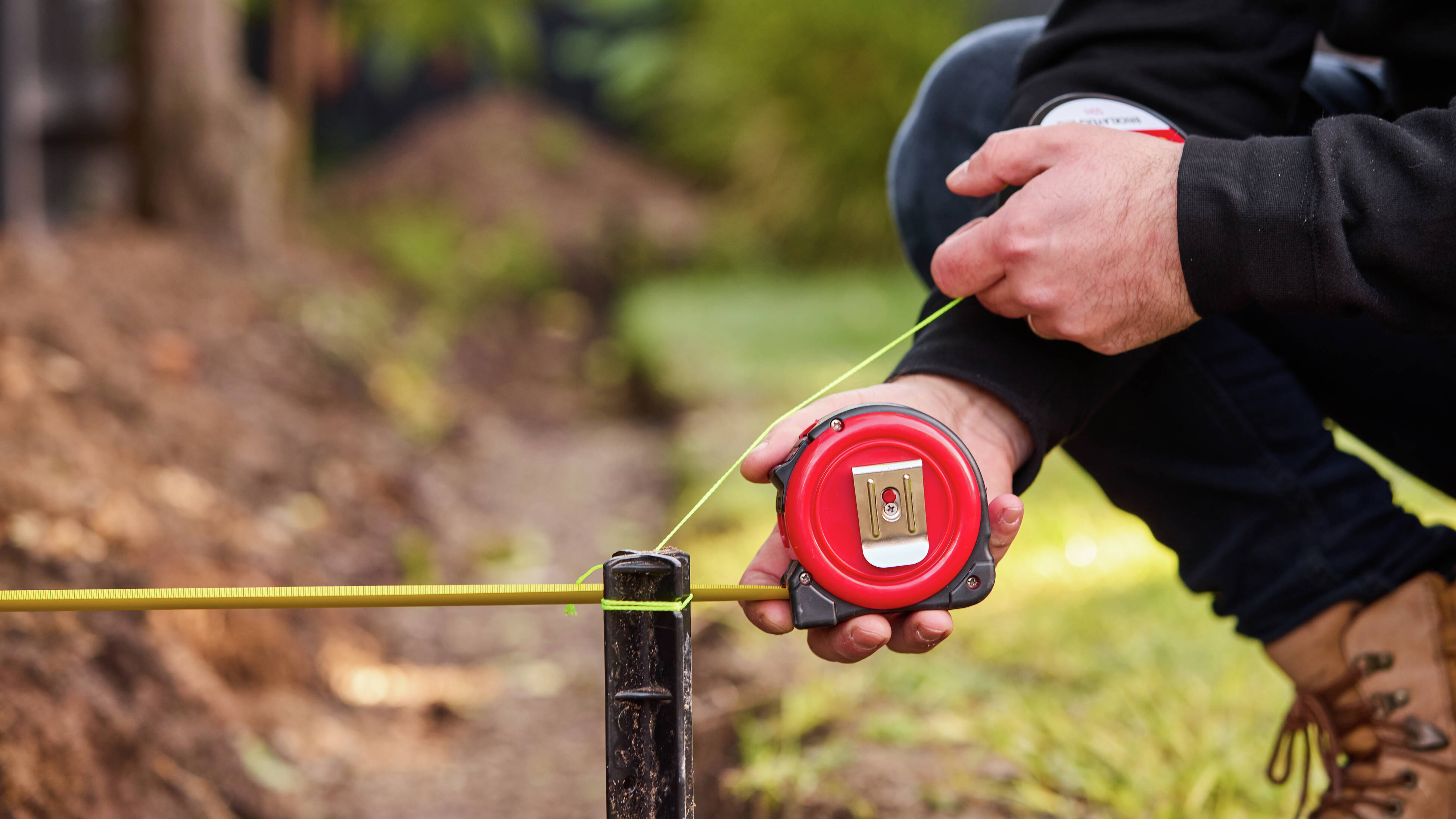 A person using a tape measure in the yard.