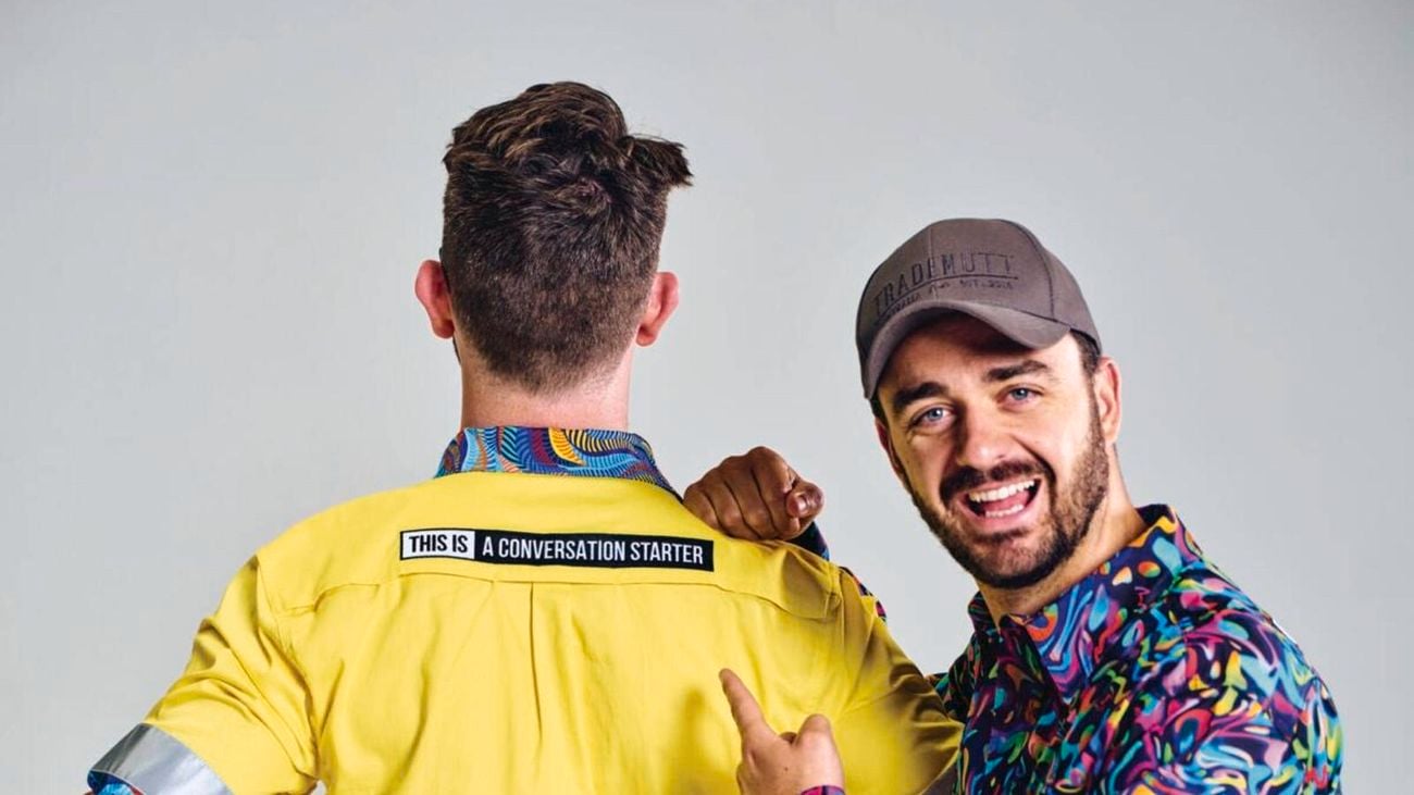 TIACS co-founder Ed Ross stands smiling and pointing to the slogan on the back of Dan Ross brightly coloured shirt