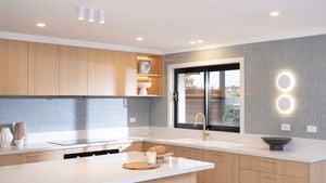 A modern kitchen features light wood cabinetry, a sleek white benchtop, vertical tile splashback, and stylish lighting.