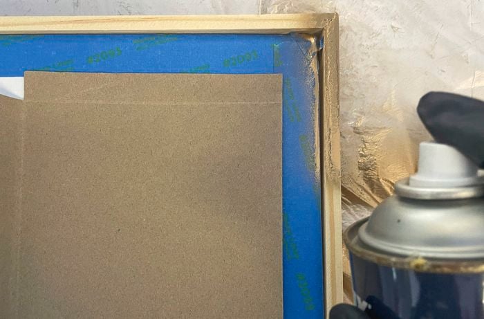 Close up image of a black gloved hand spray painting picture frames gold to make a gallery wall