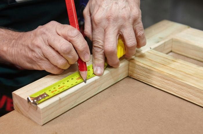 Person measuring timber with tape measure and marking it with a pencil.