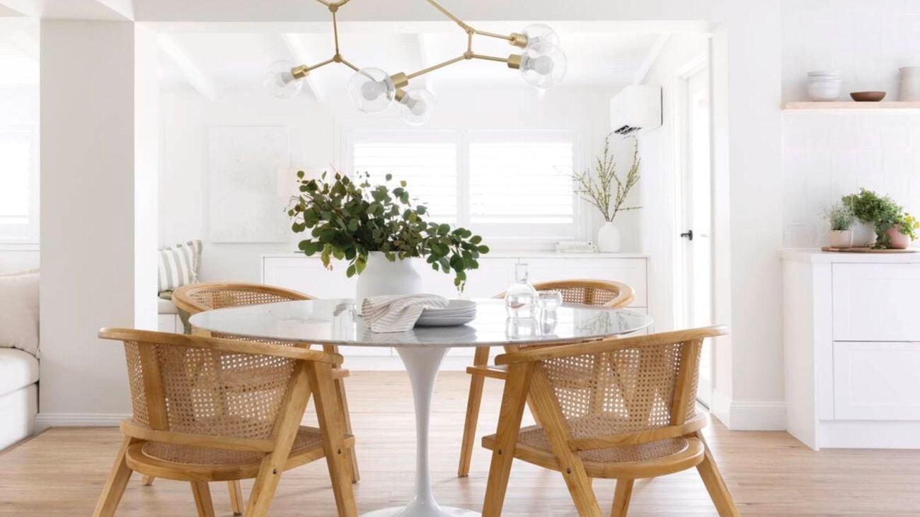 Bright, white room with a glass table, wooden chairs and a geometric gold ceiling light