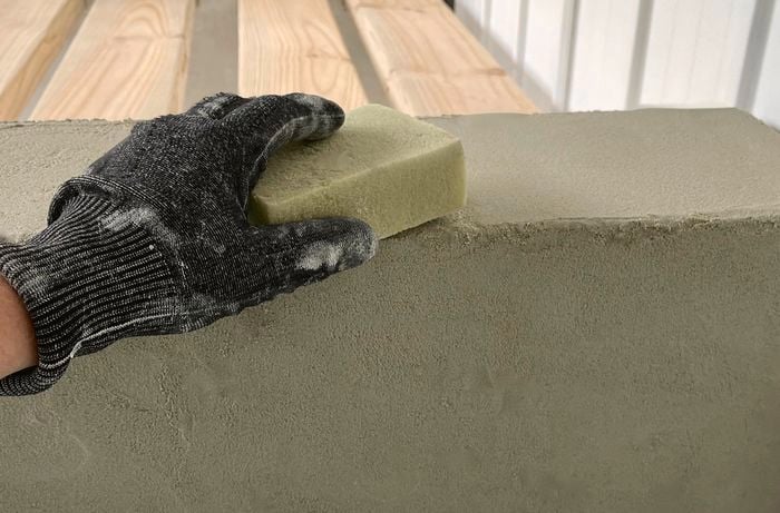 A person rubbing a damp sponge over a rendered block
