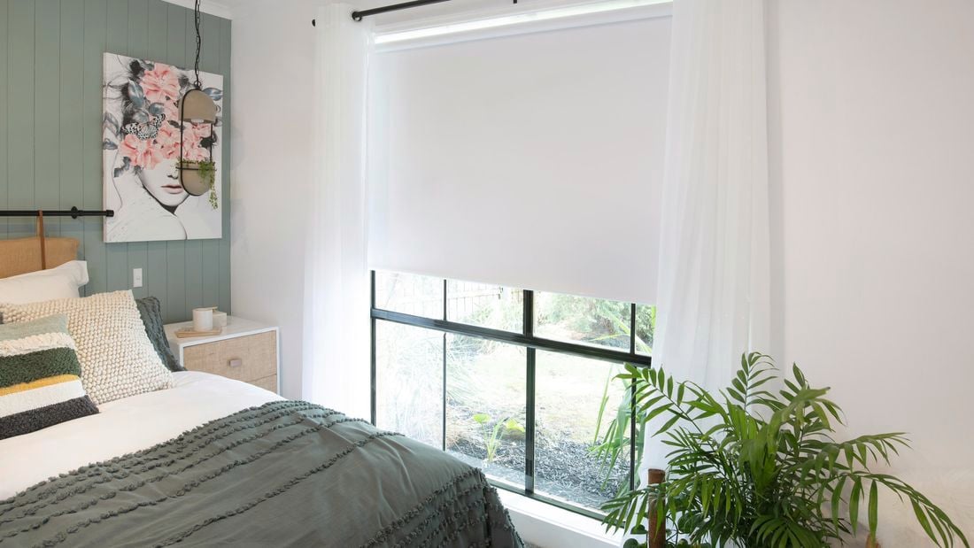 A bedroom with a white roller blind and sheer white curtains