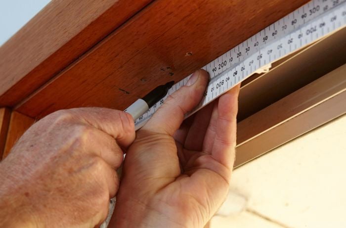Person using measuring tape and marker to markup window frame.