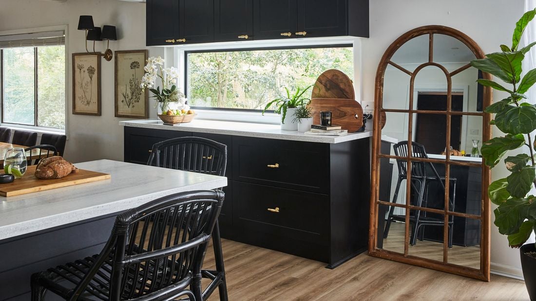 A rustic themed kitchen with black cabinets, marble countertop and wooden trim