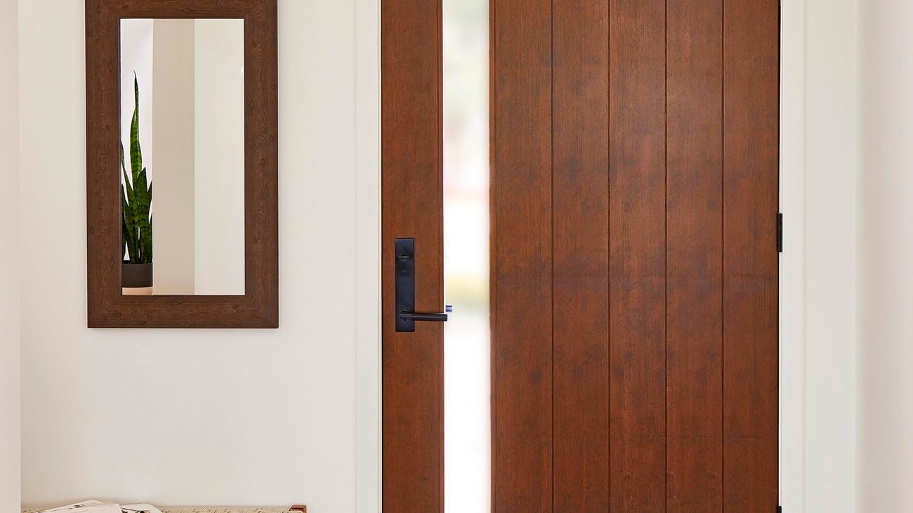 A hallway with a wooden front door, a mirror on the wall and a table next to the wall.