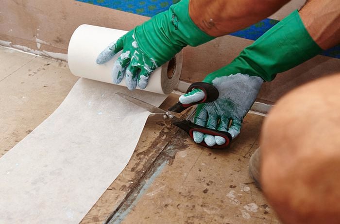 A person using scissors to cut a roll of waterproof membrane